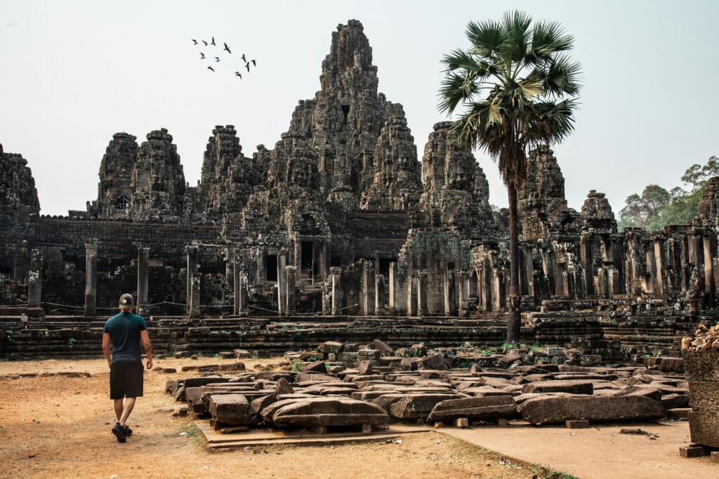 pexels-photo-2495575-2495575 Traveler exploring the ancient Bayon Temple at Angkor Thom, Cambodia, surrounded by stunning architecture.